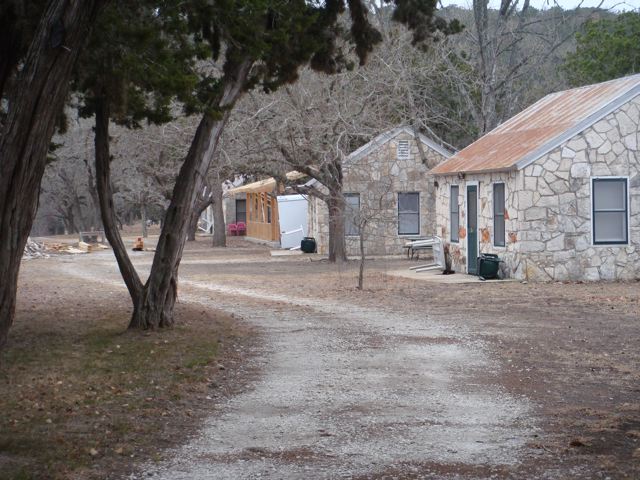 A dirt road with trees and buildings in the background.